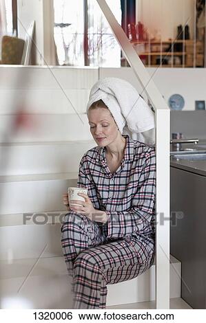 Stock Photograph - Woman holding coffee cup sitting on staircase. Fotosearch