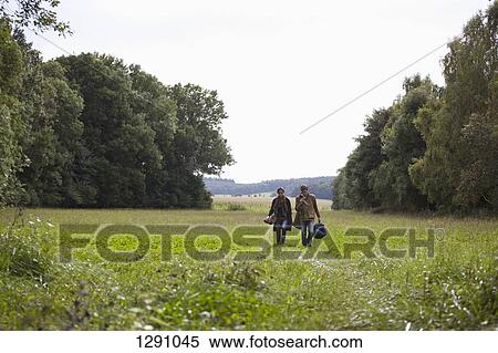 Stock Photography - Young couple carrying camping accessories walking through field. Fotosearch