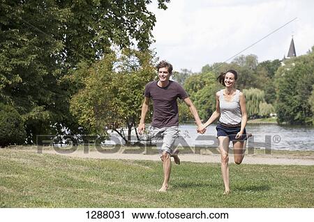 Young couple holding hands and running in park View Large Photo Image Stock Image - Young couple holding hands and running in park. Fotosearch