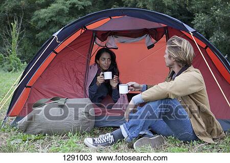 Stock Image - Young couple in dome tent having drink. Fotosearch