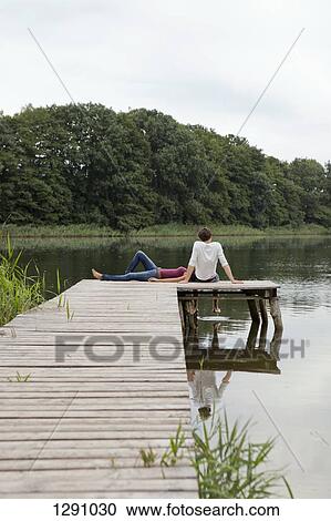 Stock Image - Young couple relaxing on pier. Fotosearch