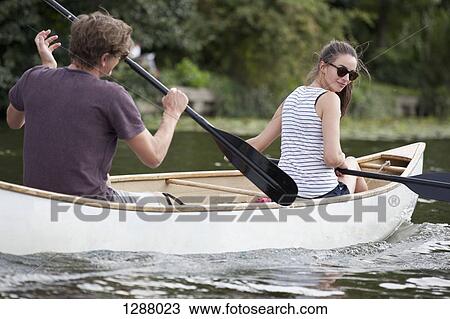 Stock Image - Young couple rowing canoe on lake. Fotosearch