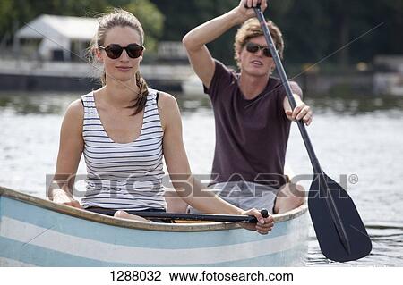 Stock Image - Young couple rowing canoe on lake. Fotosearch