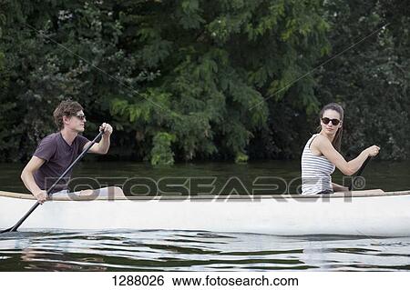 Stock Photograph - Young couple rowing canoe on lake. Fotosearch