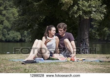 Young couple sitting on picnic blanket, holding water melon slice View Large Photo Image Stock Photo - Young couple sitting on picnic blanket, holding water melon slice. Fotosearch