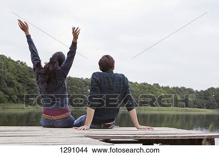 Picture - Young couple sitting on pier, rear view. Fotosearch