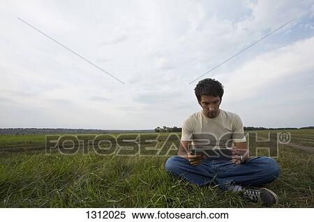 Young man sitting on grass and using digital tablet View Large Photo Image Stock Photography - Young man sitting on grass and using digital tablet. Fotosearch