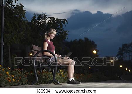 Young woman sitting on park bench and using laptop View Large Photo Image Stock Image - Young woman sitting on park bench and using laptop. Fotosearch