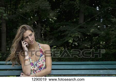 Young woman sitting on park bench using mobile phone View Large Photo Image Stock Photo - Young woman sitting on park bench using mobile phone. Fotosearch
