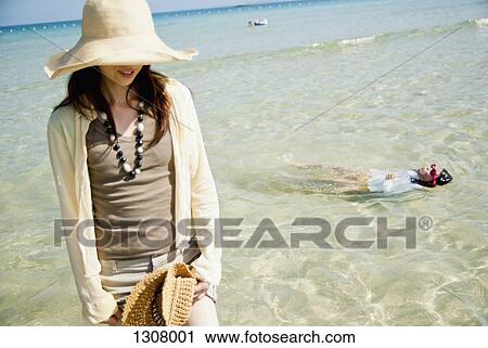 Stock Image - Young woman standing at beach. Fotosearch