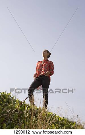 Young woman standing in park, low angle view View Large Photo Image Stock Image - Young woman standing in park, low angle view. Fotosearch