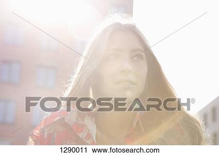 Stock Image - Young woman standing under sunshine, close-up. Fotosearch