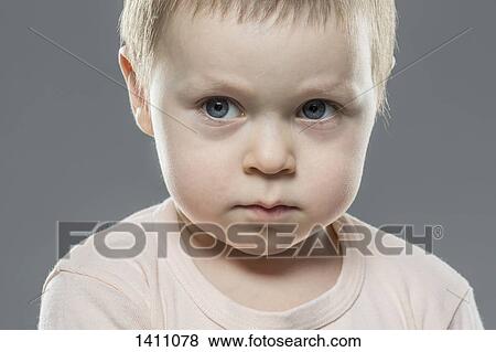 Stock Photo - Angry boy looking away against gray background. Fotosearch