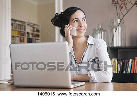 Beautiful young woman using mobile phone with laptop on table at home View Large Photo Image Stock Photography - Beautiful young woman using mobile phone with laptop on table at home. Fotosearch