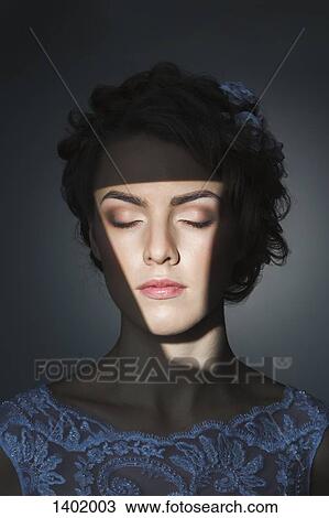 Stock Image - Beautiful young woman with eyes closed over gray background. Fotosearch