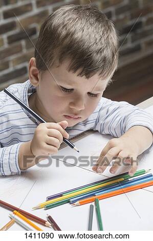 Stock Image - Boy coloring on paper at table in house. Fotosearch