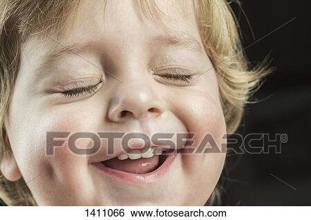 Stock Photograph - Close-up of cheerful boy with eyes closed over black background. Fotosearch