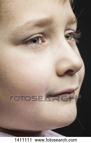 Stock Image - Close-up of thoughtful boy against black background. Fotosearch