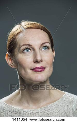Picture - Close-up of thoughtful mature woman against gray background. Fotosearch