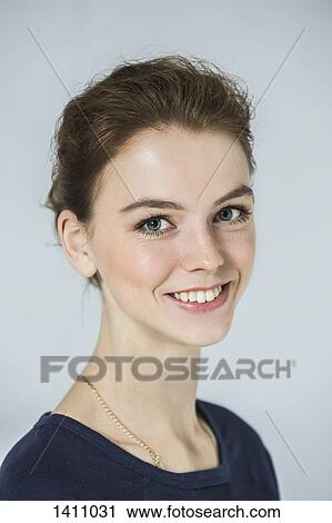 Stock Image - Close-up portrait of happy beautiful woman against gray background. Fotosearch