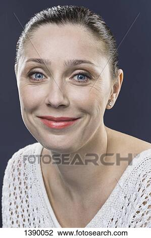 Stock Image - Close-up portrait of smiling mid adult woman over gray background. Fotosearch