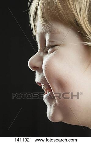 Stock Image - Close-up side view of happy boy against black background. Fotosearch