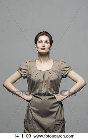 Confident fashion model standing with hands on hips against gray background View Large Photo Image Stock Photo - Confident fashion model standing with hands on hips against gray background. Fotosearch