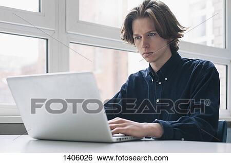 Stock Photograph - Confident young man using laptop at a desk. Fotosearch