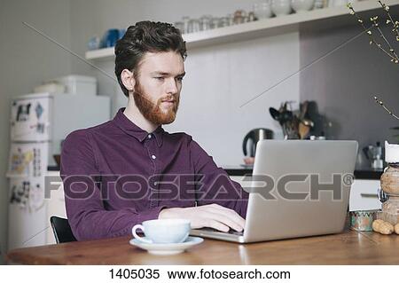 Confident young man using laptop at table in kitchen View Large Photo Image Stock Photography - Confident young man using laptop at table in kitchen. Fotosearch