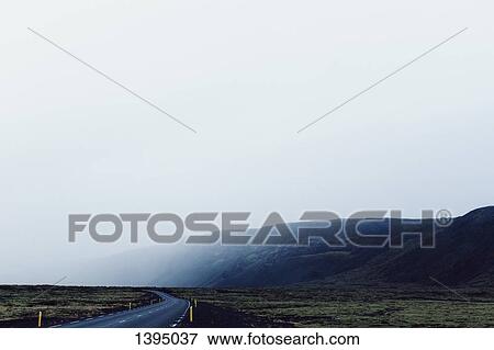 Country road passing by mountain in foggy weather against clear sky View Large Photo Image Stock Photo - Country road passing by mountain in foggy weather against clear sky. Fotosearch