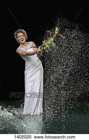 Excited young bride splashing water with bouquet against black background View Large Photo Image Stock Image - Excited young bride splashing water with bouquet against black background. Fotosearch