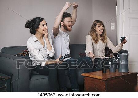 Excited young friends playing video games at home View Large Photo Image Stock Image - Excited young friends playing video games at home. Fotosearch