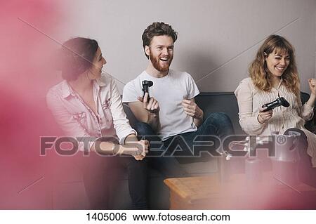 Excited young friends playing video games at home View Large Photo Image Stock Photograph - Excited young friends playing video games at home. Fotosearch