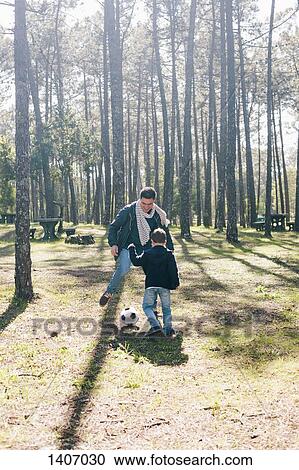 Stock Image - Father and son playing soccer in forest. Fotosearch