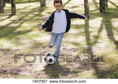 Full length of happy boy playing soccer in forest View Large Photo Image Stock Photo - Full length of happy boy playing soccer in forest. Fotosearch