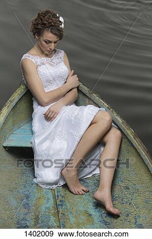 Stock Photo - Full length of young bride sitting in boat on lake. Fotosearch