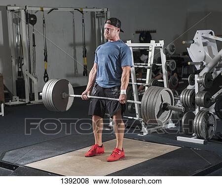 Full length of young man lifting barbell in gym View Large Photo Image Stock Photo - Full length of young man lifting barbell in gym. Fotosearch