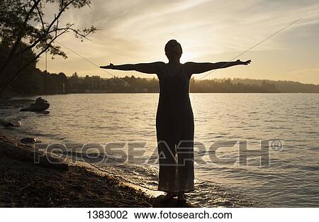 Full length of young woman standing with arms outstretched on lakeshore View Large Photo Image Stock Image - Full length of young woman standing with arms outstretched on lakeshore. Fotosearch