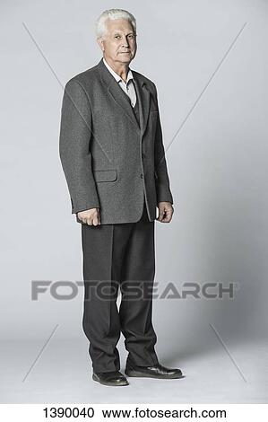 Stock Image - Full length portrait of confident senior man standing over gray background. Fotosearch