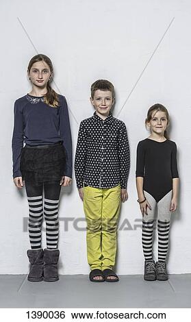 Stock Photograph - Full length portrait of smiling brother with sisters standing side by side against wall. Fotosearch