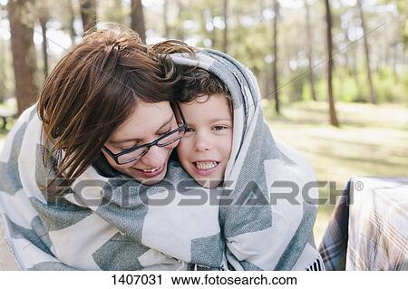 Stock Image - Happy mother and son wrapped in blanket at forest. Fotosearch