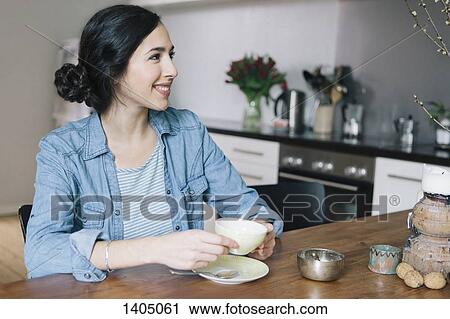 Happy young woman having coffee while looking away in kitchen View Large Photo Image Stock Image - Happy young woman having coffee while looking away in kitchen. Fotosearch
