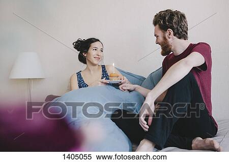 Happy young woman holding birthday cupcake with candle while looking at man on bed View Large Photo Image Stock Photography - Happy young woman holding birthday cupcake with candle while looking at man on bed. Fotosearch