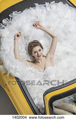 Picture - High angle view of young bride in wedding dress sitting in convertible. Fotosearch