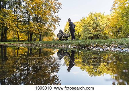 Stock Image - Mother walking with baby stroller in park. Fotosearch