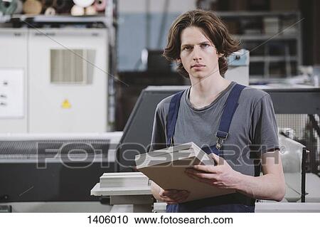 Stock Image - Portrait of confident manual worker holding cardboard sheets in factory. Fotosearch