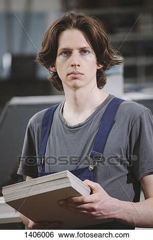 Stock Photograph - Portrait of confident manual worker holding cardboard sheets in a factory. Fotosearch