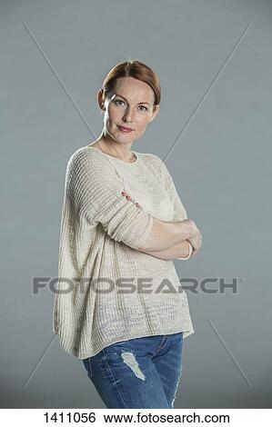 Stock Photograph - Portrait of confident woman standing arms crossed against gray background. Fotosearch