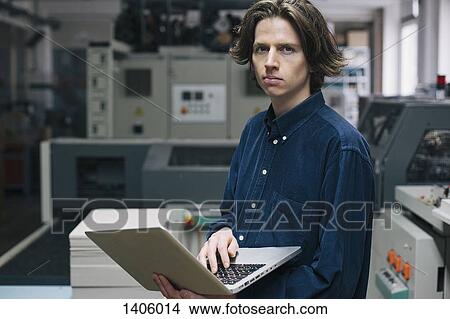 Picture - Portrait of confident young male technician using laptop in factory. Fotosearch