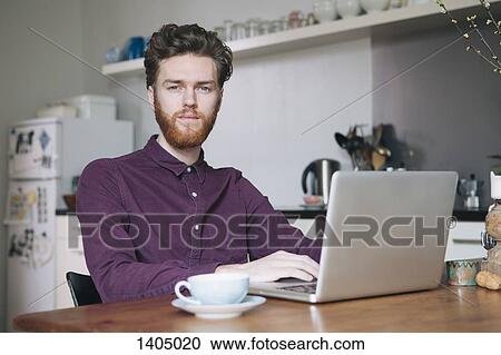 Portrait of confident young man using laptop at table in kitchen View Large Photo Image Stock Image - Portrait of confident young man using laptop at table in kitchen. Fotosearch